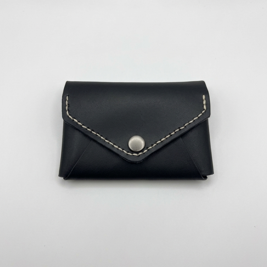 Black leather cardholder with silver button on a light gray background -  AERA Berlin