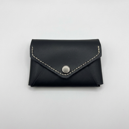 Black leather cardholder with silver button on a light gray background -  AERA Berlin