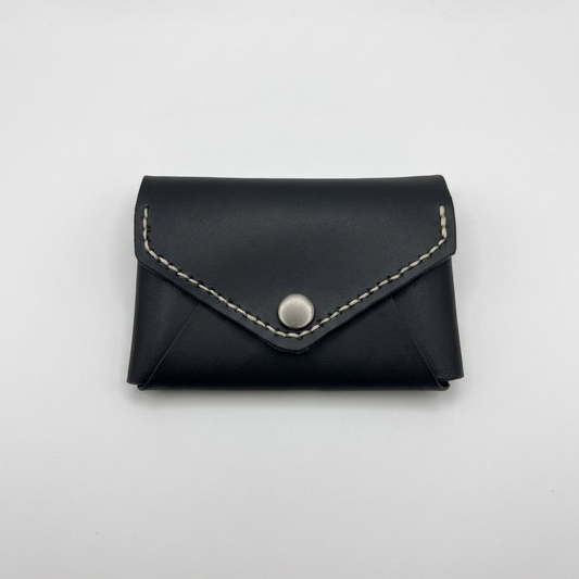 Black leather cardholder with silver button on a light gray background -  AERA Berlin